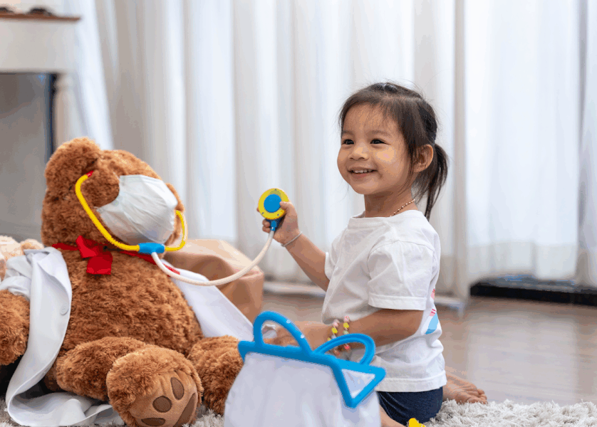 menina sentada brincando com urso e outros brinquedos.