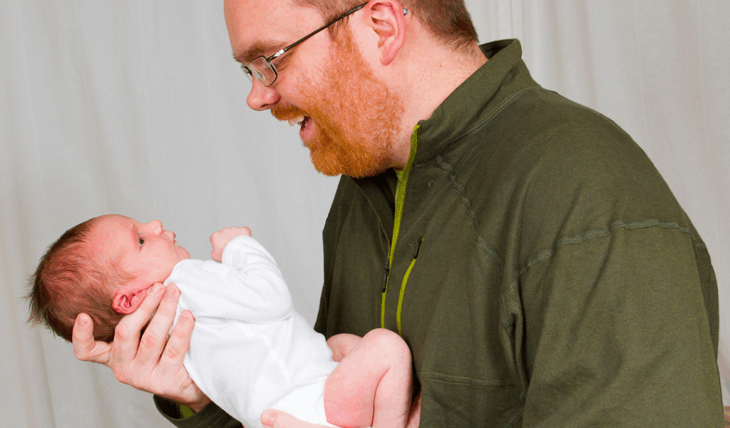 pai segurando filho recém nascido e interagindo com ele